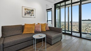 A modern living room with a grey sofa, a small round table, and a large window offering a city view. - The Pinnacle Carlton 69th Floor City Views (Carlton)
