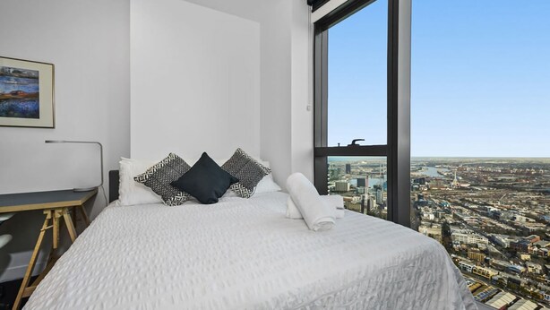 A modern hotel room with a large bed, a desk, and a view of a cityscape through a large window. - The Pinnacle Carlton 69th Floor City Views (Carlton)