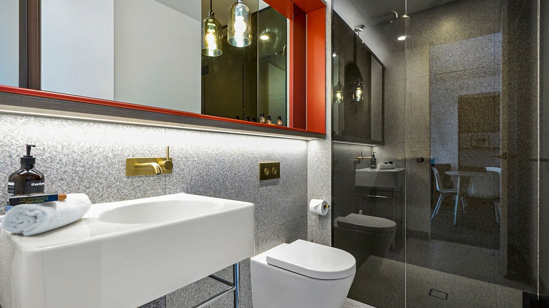 Un bagno moderno con un lavandino bianco, un rubinetto dorato, un WC e un box doccia in vetro.