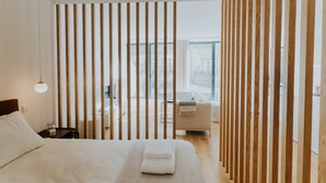 A modern hotel room with a large bed, a nightstand, a lamp, and a view of the city through large windows. - VIVA Formosa Lofts 1 (Porto)