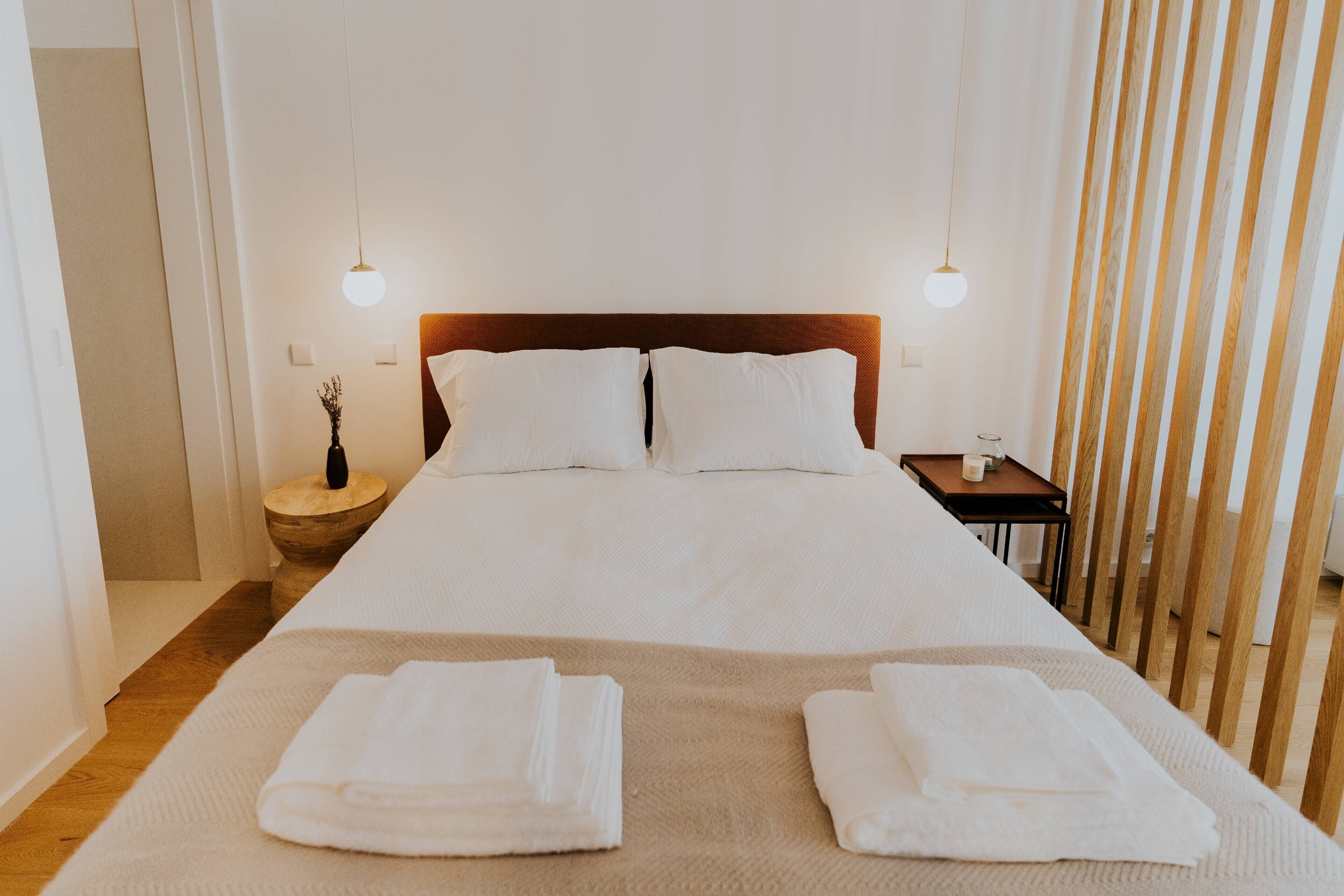 A neatly made bed with white linens, two bedside tables with candles, and a wooden floor.
