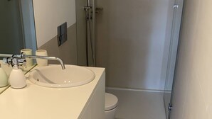 A modern bathroom with a white sink, toilet, and shower. A beige rug is placed on the floor. - VIVA Formosa Lofts 1 (Porto)