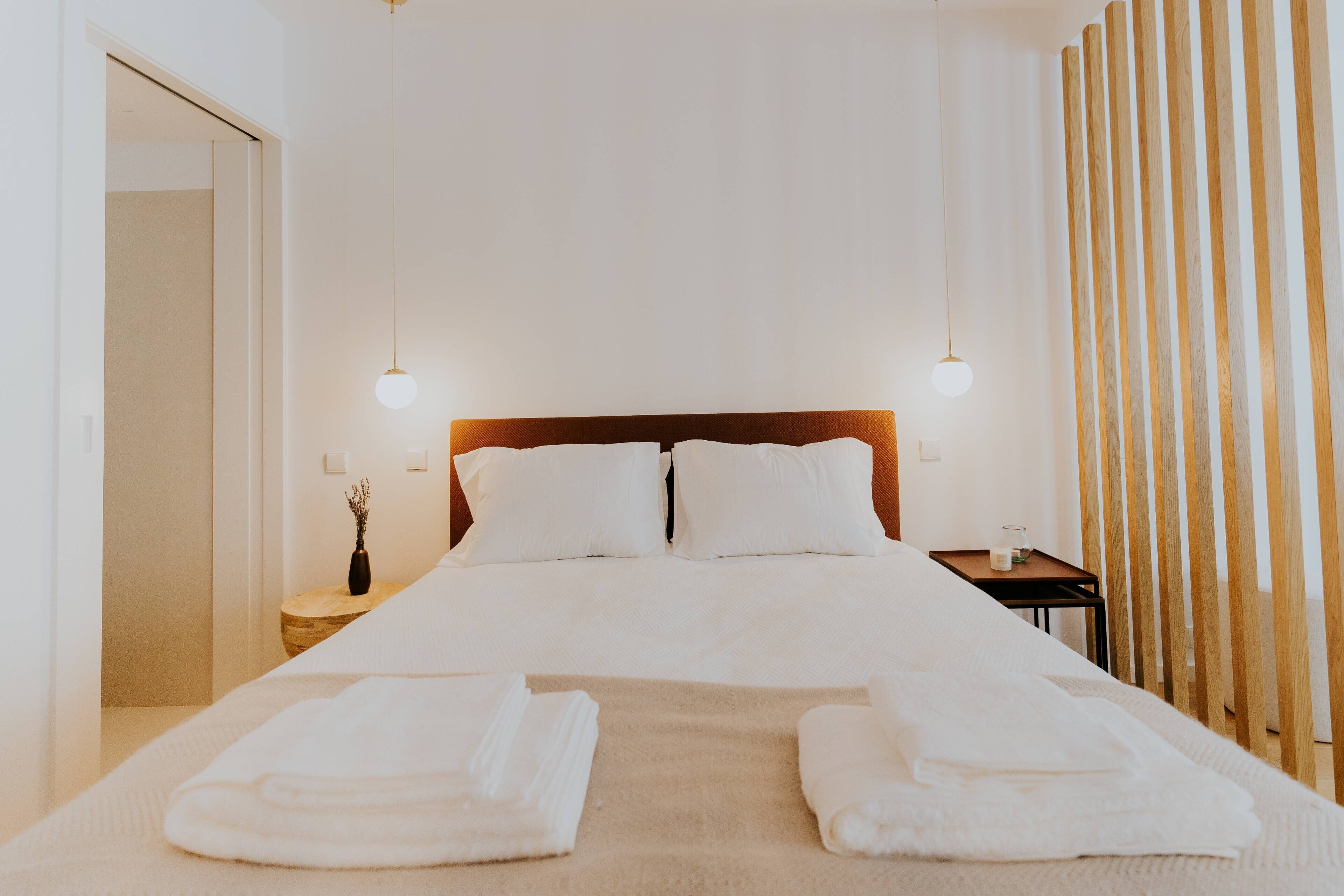 A hotel room with a large bed, two bedside tables, a wooden headboard, and a wooden slat partition.