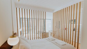 A modern bedroom with a large bed, a bedside lamp, and a view through a wooden partition. - VIVA Formosa Lofts 1 (Porto)