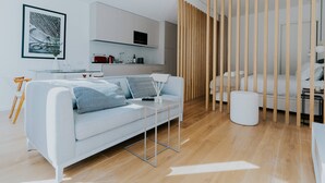 A modern living room with a sofa, a coffee table, a dining table, and a kitchen area in the background.