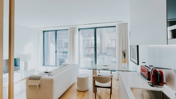 A modern living room with a sofa, a glass dining table, and a kitchen area with a toaster.