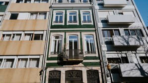 Ein mehrstöckiges Gebäude mit einer grün-beigen Fassade, mehreren Balkonen und blauem Himmel.