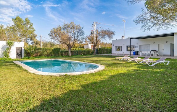 A swimming pool with lounge chairs, a modern house, and a clear sky.