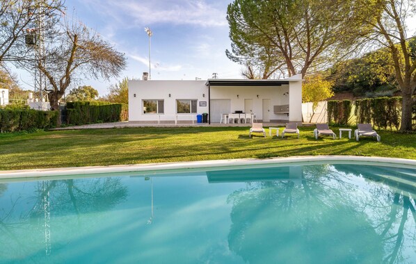 Una casa moderna con piscina, un patio con sillones de descanso y un césped cuidado.