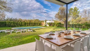 Un área de comedor al aire libre con piscina, sillas blancas y una mesa dispuesta para seis personas.