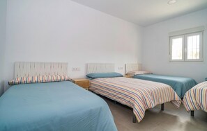 A room with three beds, each with striped bedding, wooden headboards, and a window providing natural light.