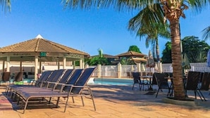 Ett område vid poolen med solstolar, en möblerad sittgrupp under tak och en palm.