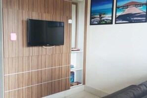 Ein Zimmer mit einem an einer Holzwand montierten Fernseher, einem Bücherregal und einem Gemälde, das eine Strandansicht zeigt.