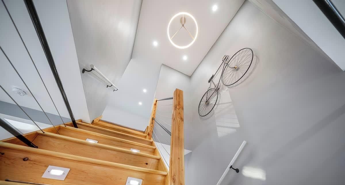 A modern interior with a wooden staircase, recessed ceiling lights, and a bicycle mounted on the wall.