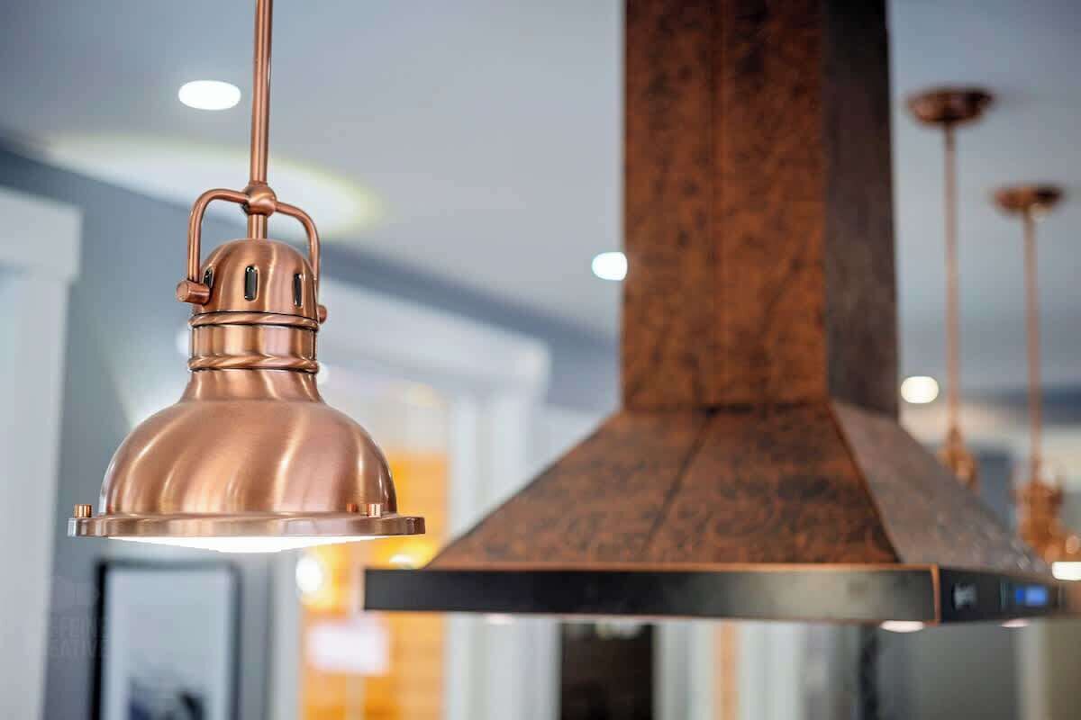 Una cocina moderna con campana extractora de cobre e iluminación colgante.