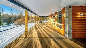 A wooden deck with a glass railing, a stone wall, and a view of a snowy landscape.