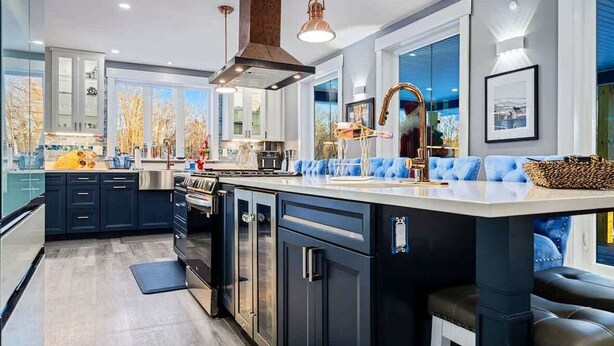 A modern kitchen with dark cabinetry, a central island, pendant lighting, and a large window.