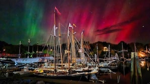 A marina with several sailboats docked, a docked yacht, and a backdrop of the Northern Lights.