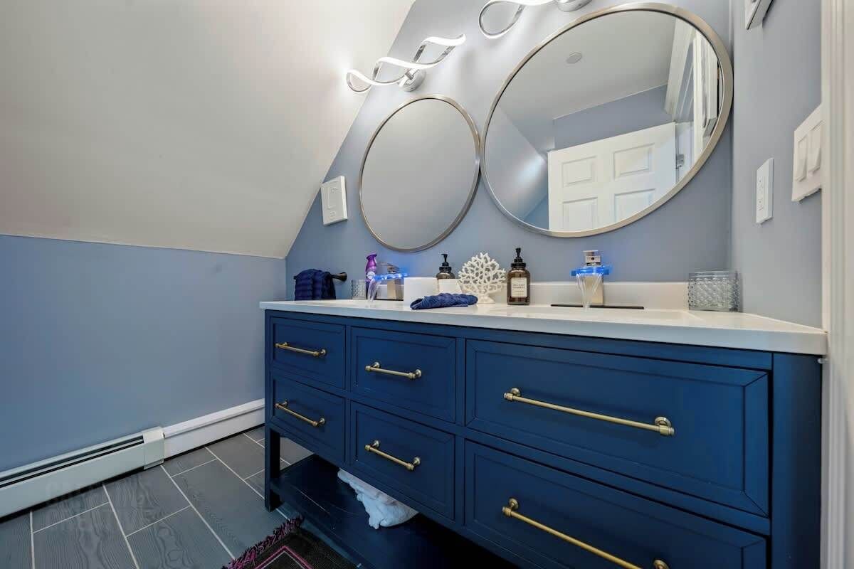 Une salle de bain avec un meuble-lavabo, deux miroirs et des articles de toilette.