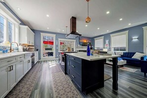 A modern kitchen with white cabinets, a central island, and a dining area with a blue couch.