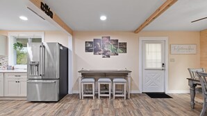 Une cuisine moderne avec un réfrigérateur en acier inoxydable, une table à manger en bois avec trois chaises et une œuvre d’art accrochée au mur.