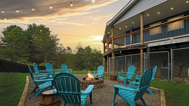 Un espace extérieur aménagé avec des chaises Adirondack et un foyer, entouré d’une terrasse en bois et d’un sol en gravier.