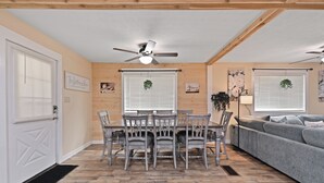 Un coin repas avec une table et des chaises, un ventilateur de plafond et un canapé gris, dans une pièce aux murs en bois et au sol orné d’un motif en chevrons.