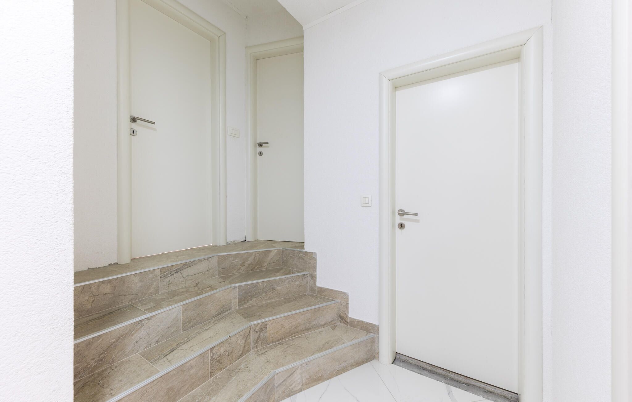 Un escalier aux marches en marbre beige menant à une porte blanche.