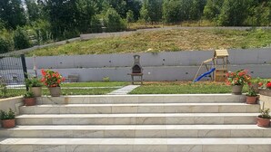 A set of marble steps leading to a patio area with a barbecue grill, a children's play structure, and potted plants. - Stunning home in Sinj (Sinj)
