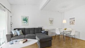 En moderne stue med en grå hjørnesofa, et hvidt sofabord og et spiseområde med et hvidt bord og stole.