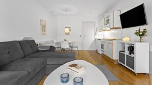 En moderne stue med en grå sofa, et hvidt sofabord med to blå glas, samt et spiseområde med et hvidt bord og stole.
