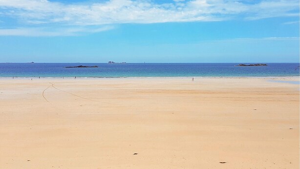 Una extensa playa de arena con cielo azul despejado y mar tranquilo.