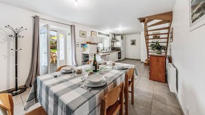Un comedor con mantel a cuadros, sillas de madera y vistas a la cocina y al jardín a través de una puerta abierta.