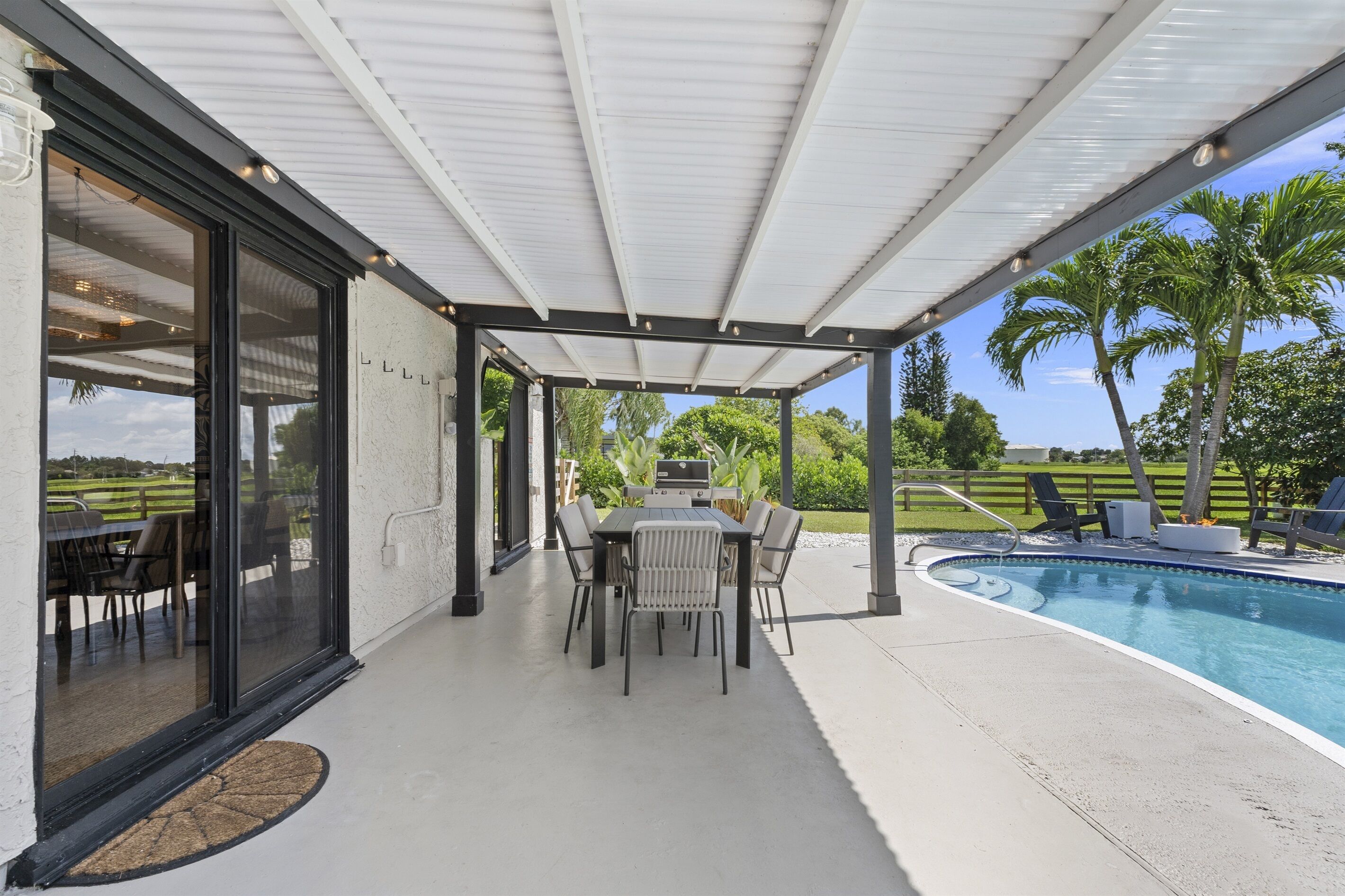 A covered patio with a pool, outdoor dining area, and a view of a golf course.