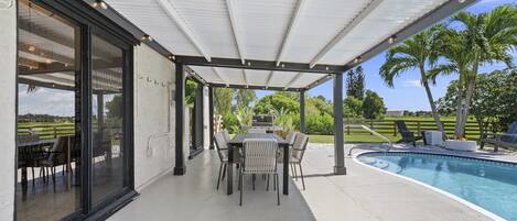 A covered patio with a pool, outdoor dining area, and a view of a golf course.