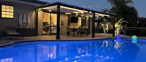 Una piscina con un porche techado, una mesa de comedor y sillas.