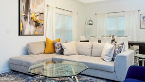 A modern living room with a beige sofa, a glass coffee table, and a large abstract painting on the wall. - Go!#05 - CHAMPIONS GATE (Kissimmee)