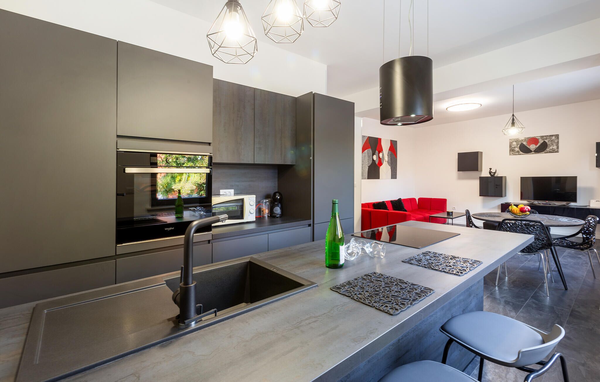 A modern kitchen with a central island, stainless steel appliances, and a red sofa in the living area.
