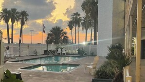A pool area with lounge chairs and palm trees, surrounded by a white fence.