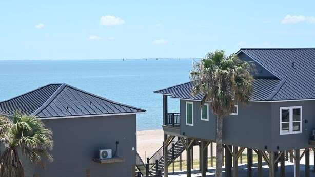 A beachfront property with two buildings, one elevated on stilts with a balcony, and another with a flat roof.