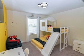 Een stapelbed met een glijbaan, een bureau, een stoel en een klein dressoir.