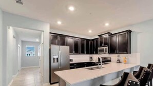 A modern kitchen with dark cabinets, stainless steel appliances, and a large island with bar stools. - Go!#14 - CHAMPIONS GATE (Kissimmee)