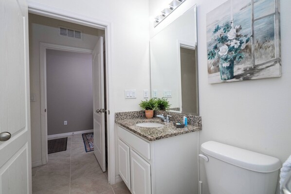 A bathroom with a sink, mirror, toilet, and a door leading to another room.