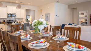 Een eethoek met een houten tafel gedekt voor vier personen, omringd door stoelen. Op de tafel staat een vaas met bloemen, en er is een moderne keuken op de achtergrond te zien.