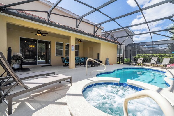 A covered outdoor pool area with lounge chairs, a hot tub, and a patio with outdoor furniture.