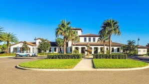A large, two-story house with a central courtyard, surrounded by palm trees and a well-maintained lawn. - Go!#30 - WINDSOR AT WESTSIDE (Kissimmee)