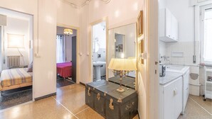 Habitación de hotel con cama, maleta, baño con lavamanos y espejo, y pasillo que conduce a otra habitación.