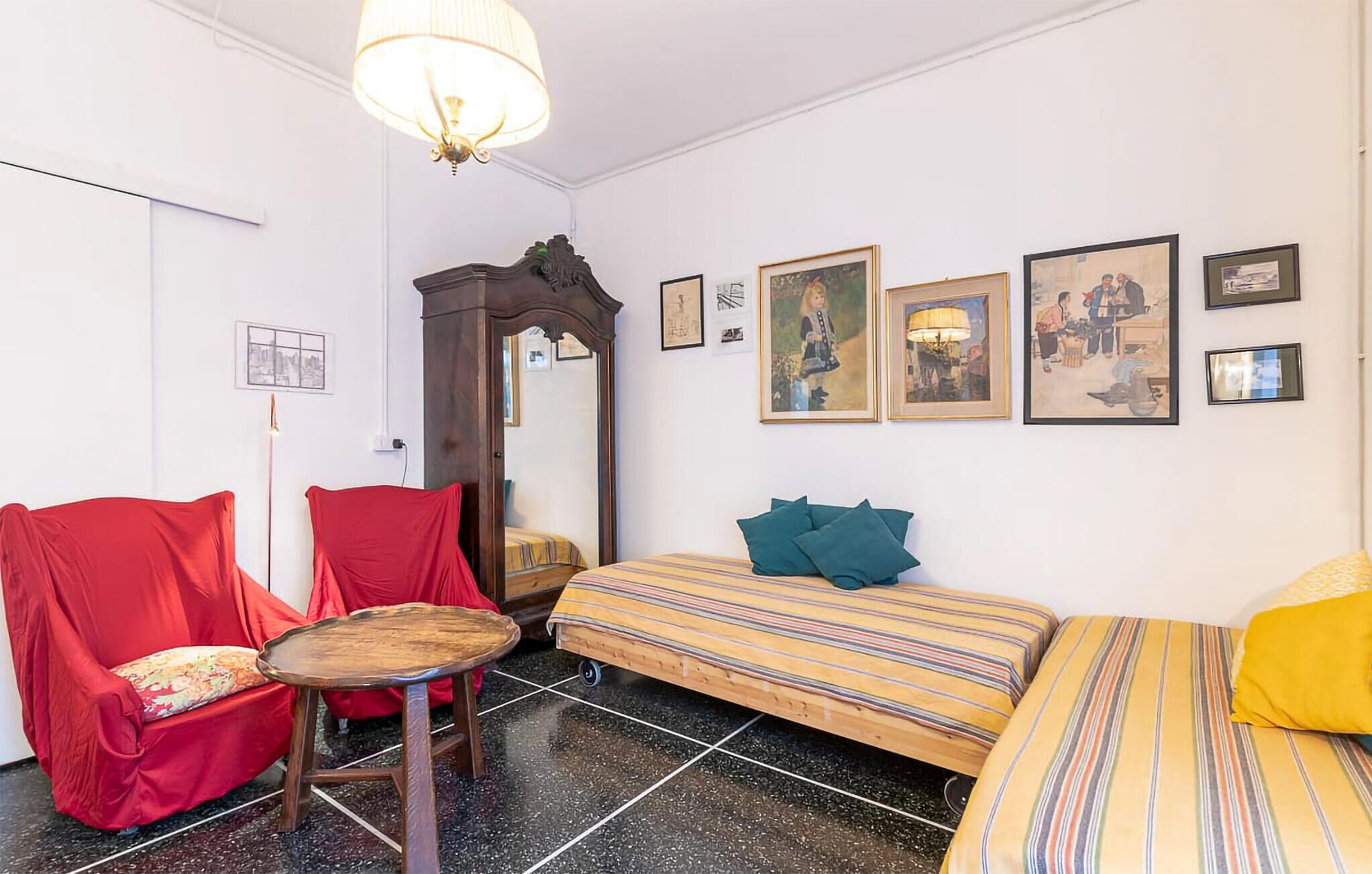 Une pièce avec un lit, une chaise, une table et un canapé. Il y a des tableaux accrochés au mur.