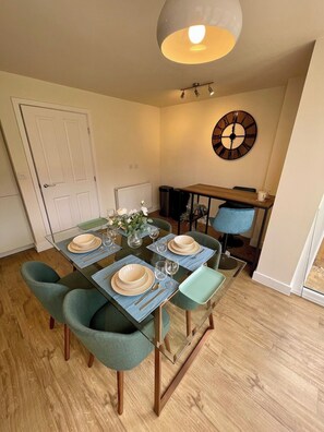 A dining area with a glass table, teal chairs, and a clock on the wall.
