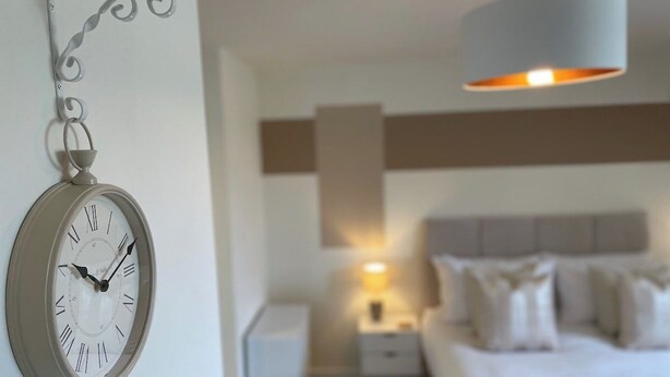 Un dormitorio con una cama, una mesita de noche, un reloj en la pared y una lámpara colgante.